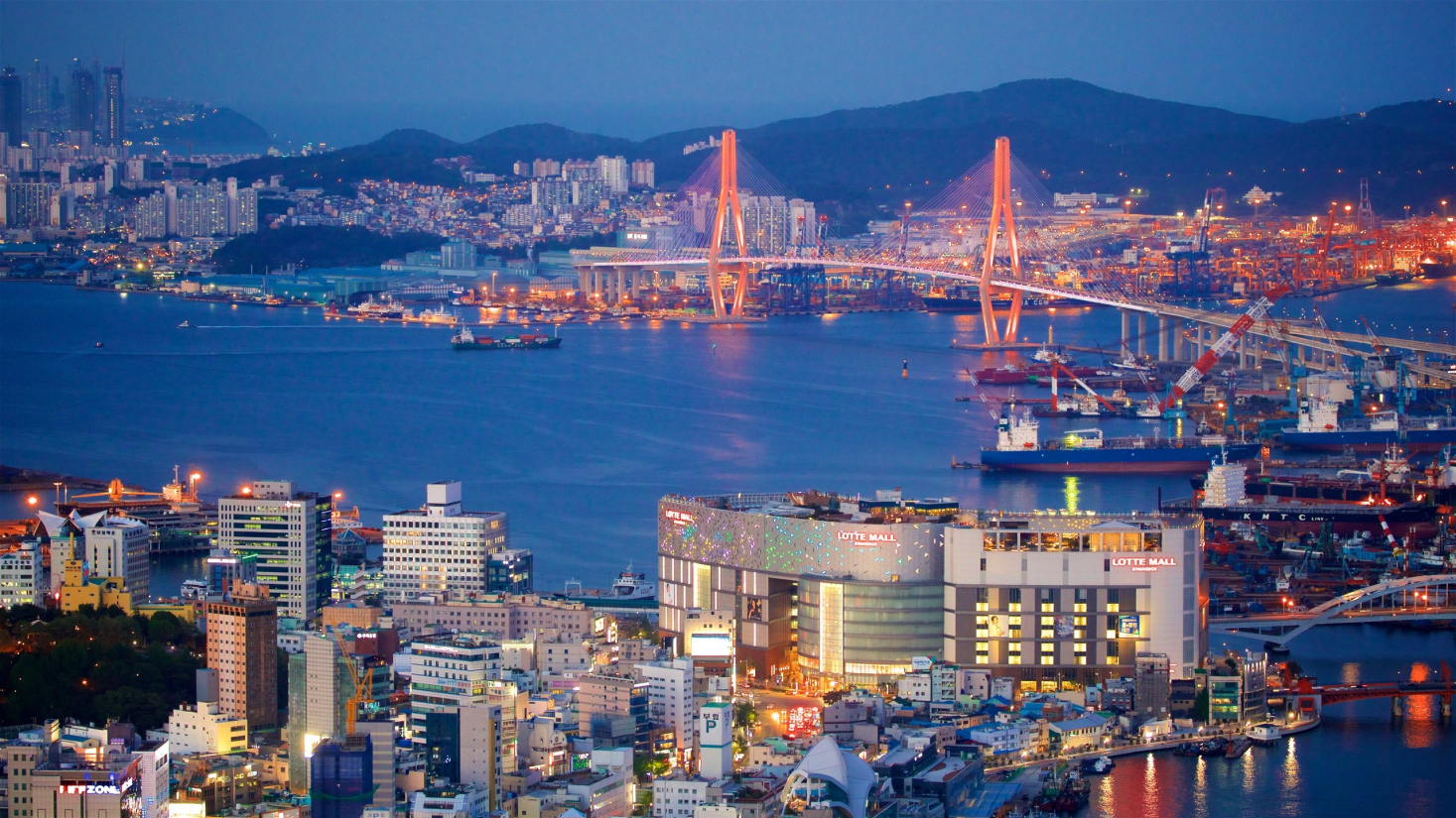 Imagem da cidade de Busan, na Coreia do Sul, mostra uma ponte, um porto de navios cargueiros, prédios, montanhas e o mar cortando a cidade ao meio.